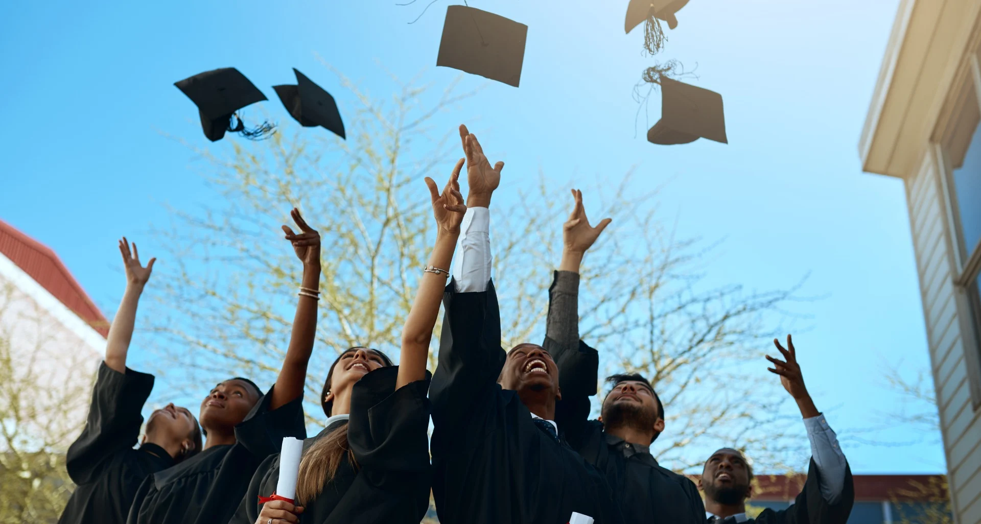 Graduates joyfully toss caps in the air, celebrating achievements beneath a clear sky, symbolizing future endeavors as home builders.