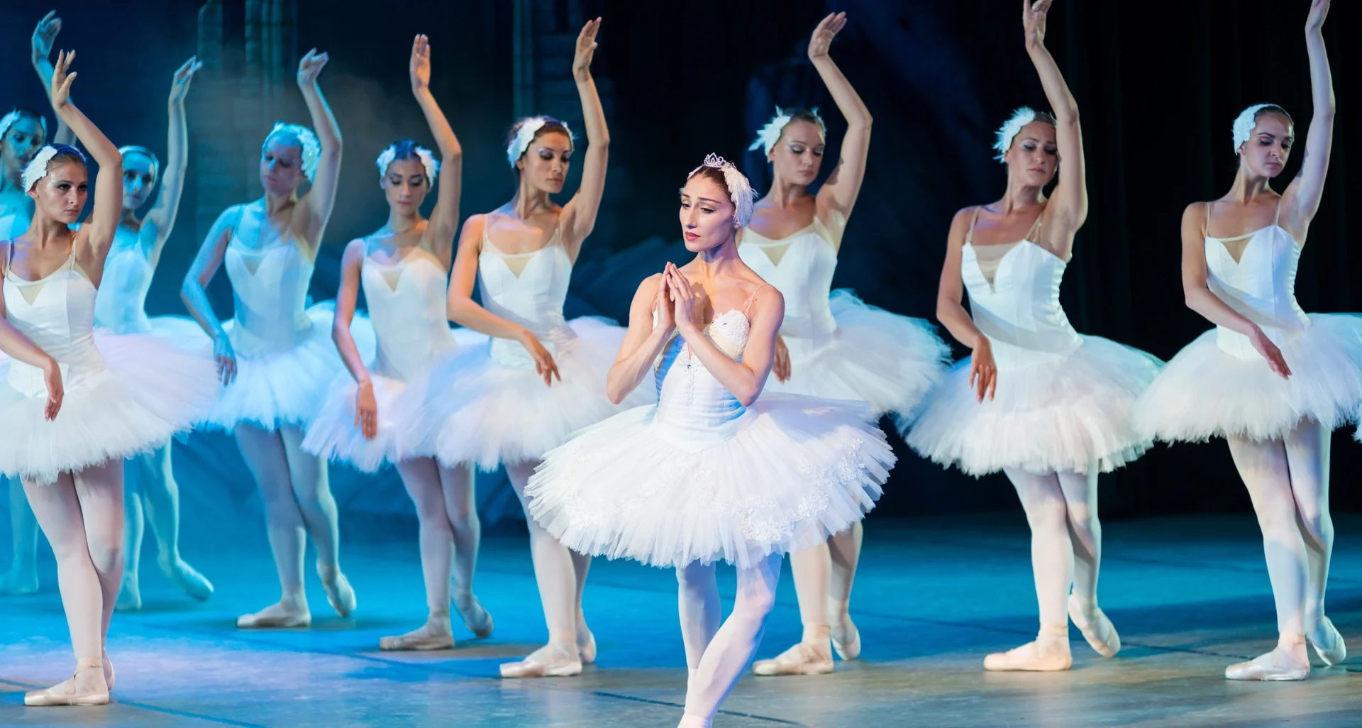 Ballet dancers in white tutus perform gracefully on stage, arms poised elegantly, evoking the precision of a home builder's delicate craftsmanship.