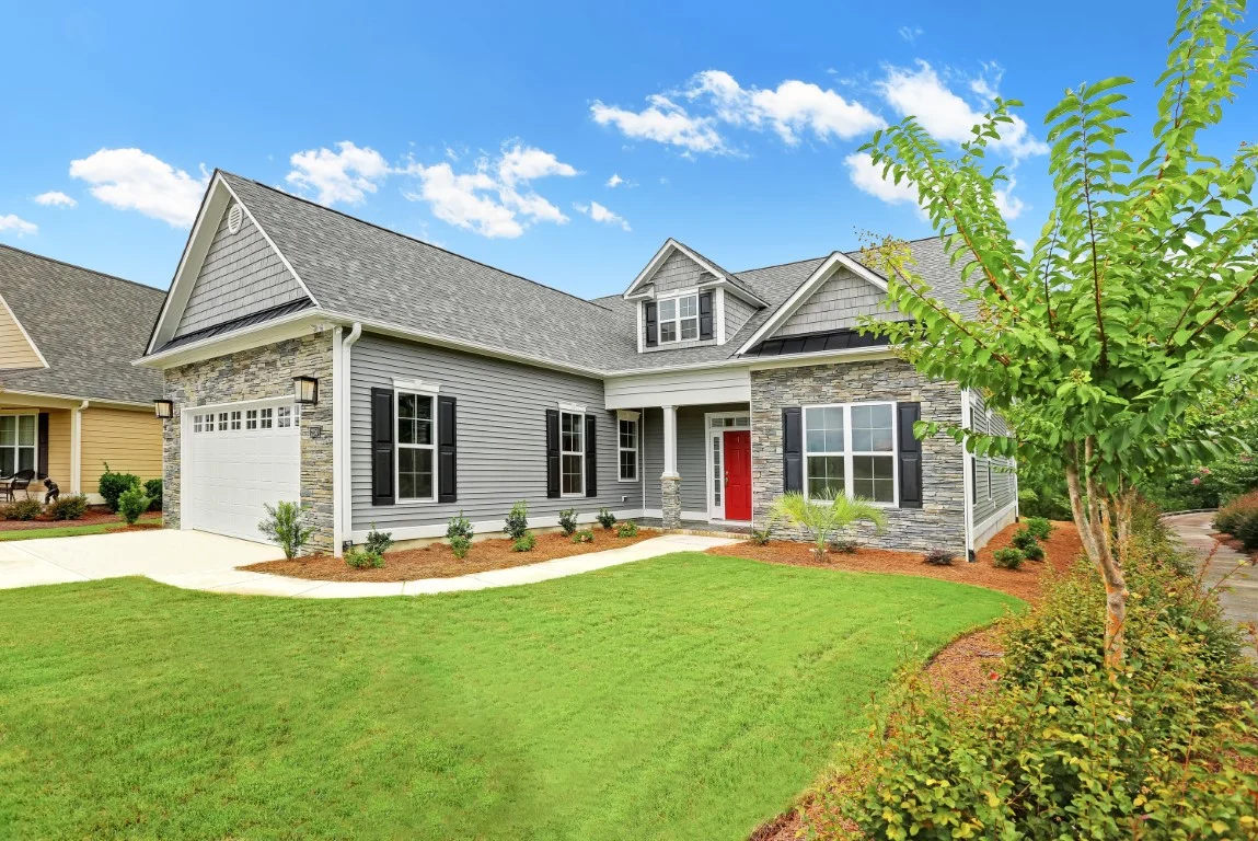 Modern home with vinyl siding, stone facade, red door, manicured lawn, and garage. Showcasing quality craftsmanship by a home builder.
