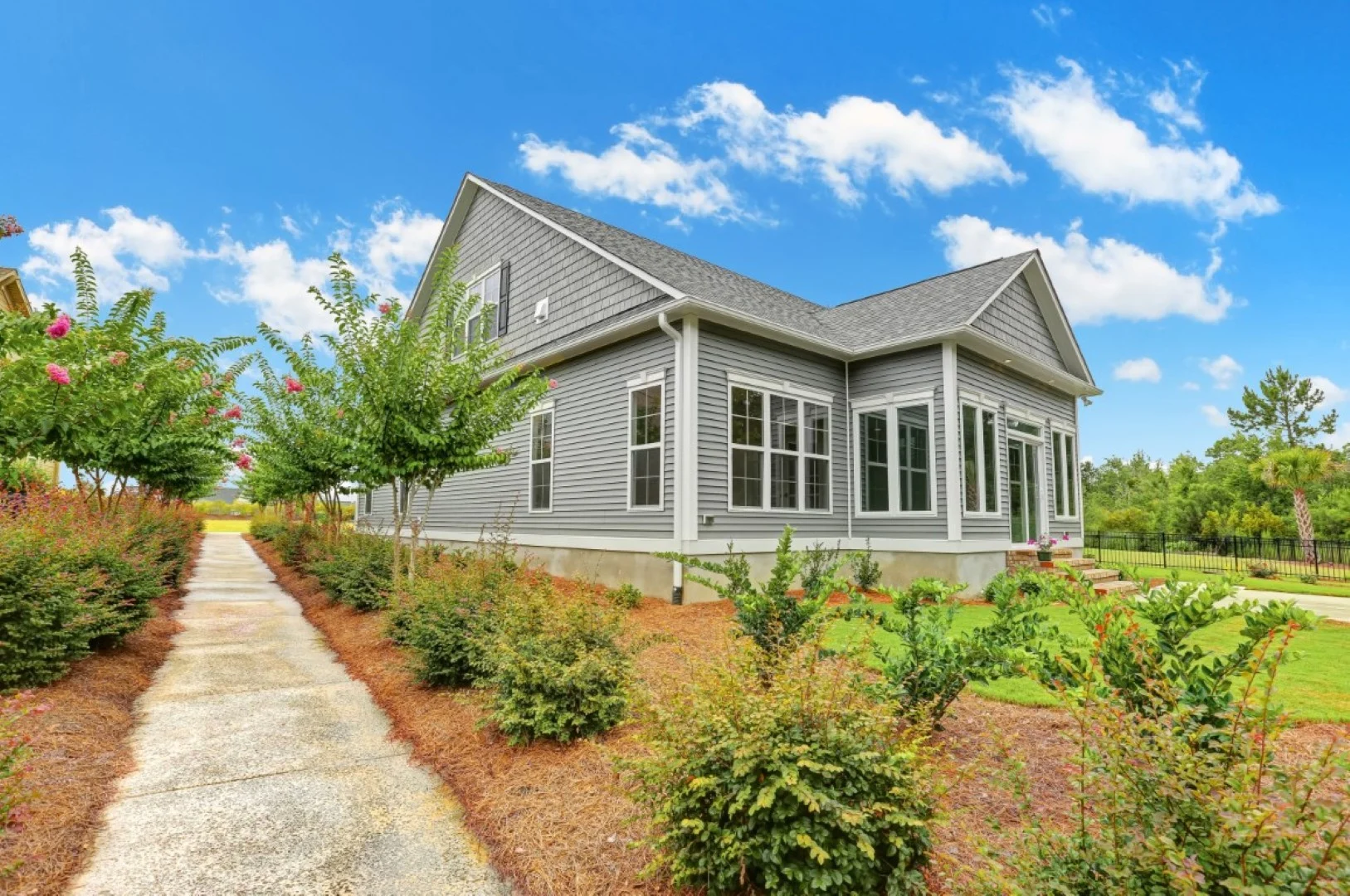 Modern gray house with large windows, surrounded by lush greenery and a clear blue sky, showcasing home builder craftsmanship.