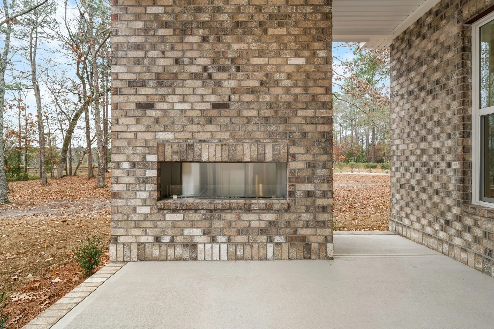 Outdoor brick wall with a built-in fireplace on a patio, surrounded by trees in autumn. Ideal design for a home builder project.