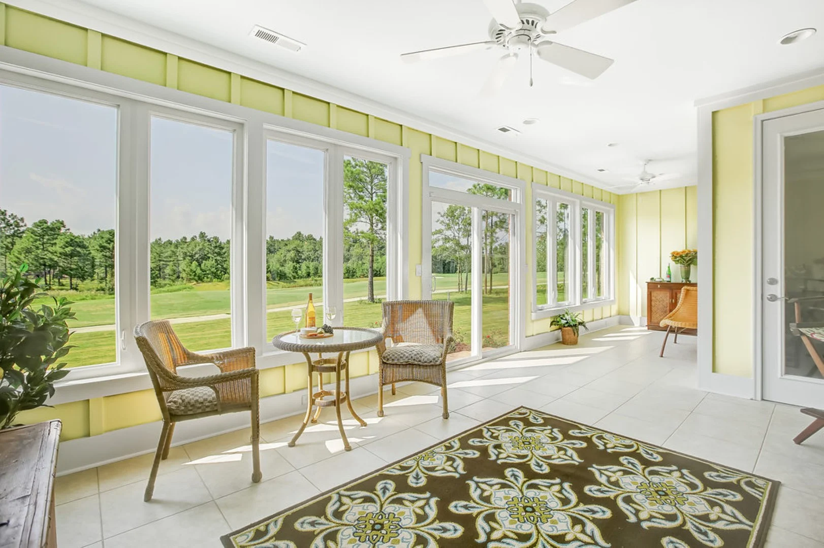 Bright sunroom with large windows overlooking a garden, featuring wicker chairs and table, by a skilled home builder.
