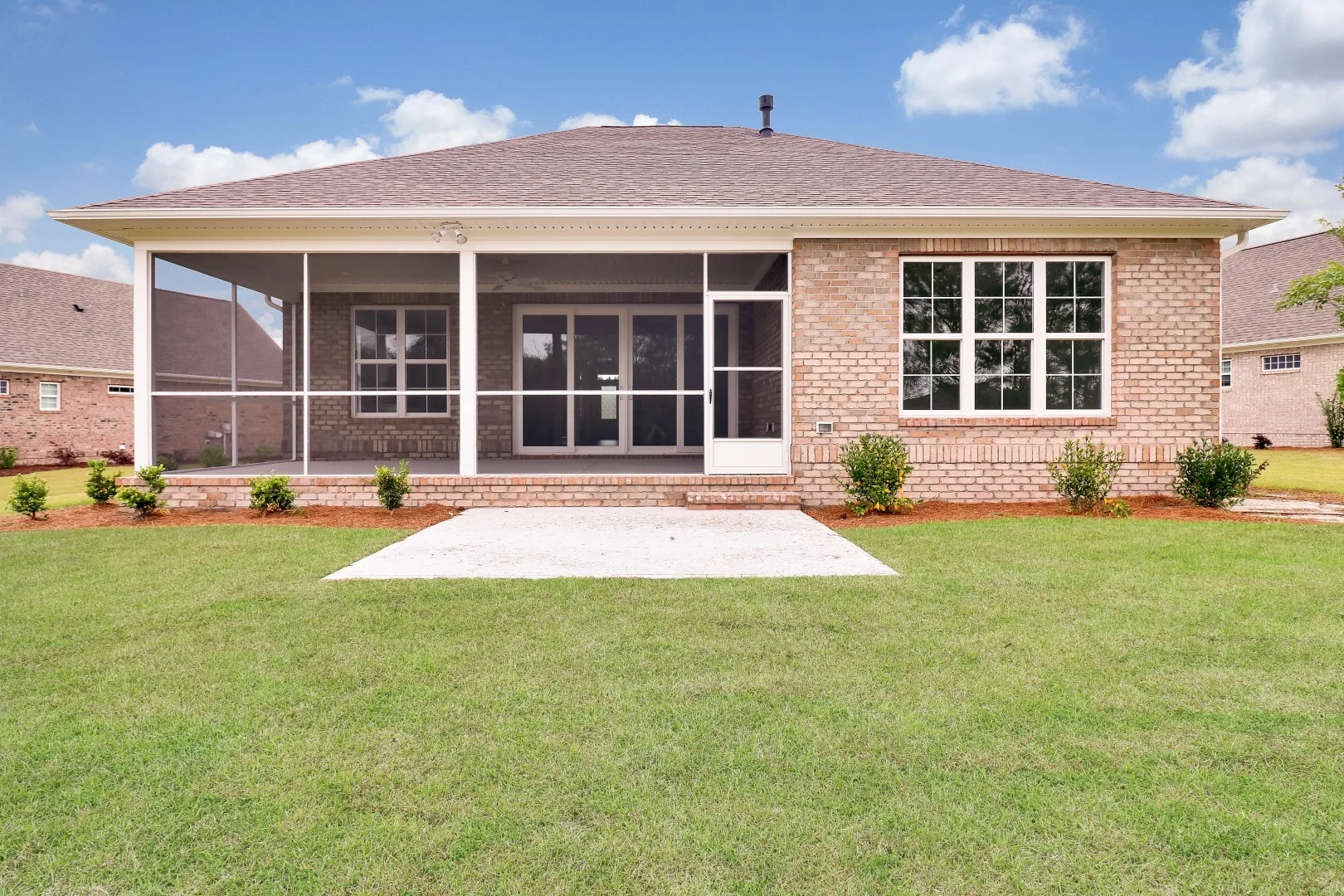 Backyard view of a brick house with a screened porch, well-maintained lawn, and young shrubs, crafted by a professional home builder.