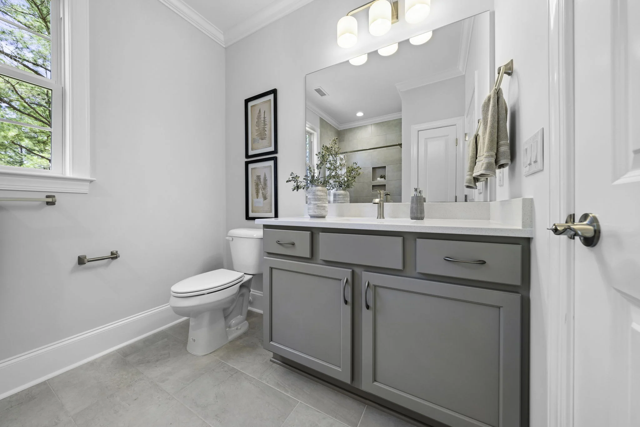 Modern bathroom with gray vanity, large mirror, and white tiles. Elegant design by home builder emphasizes natural light and minimalism.
