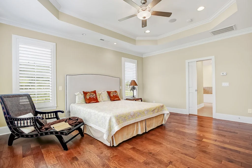 Elegant bedroom with a large bed, ceiling fan, armchair, and wooden floor, showcasing the craftsmanship of a home builder.