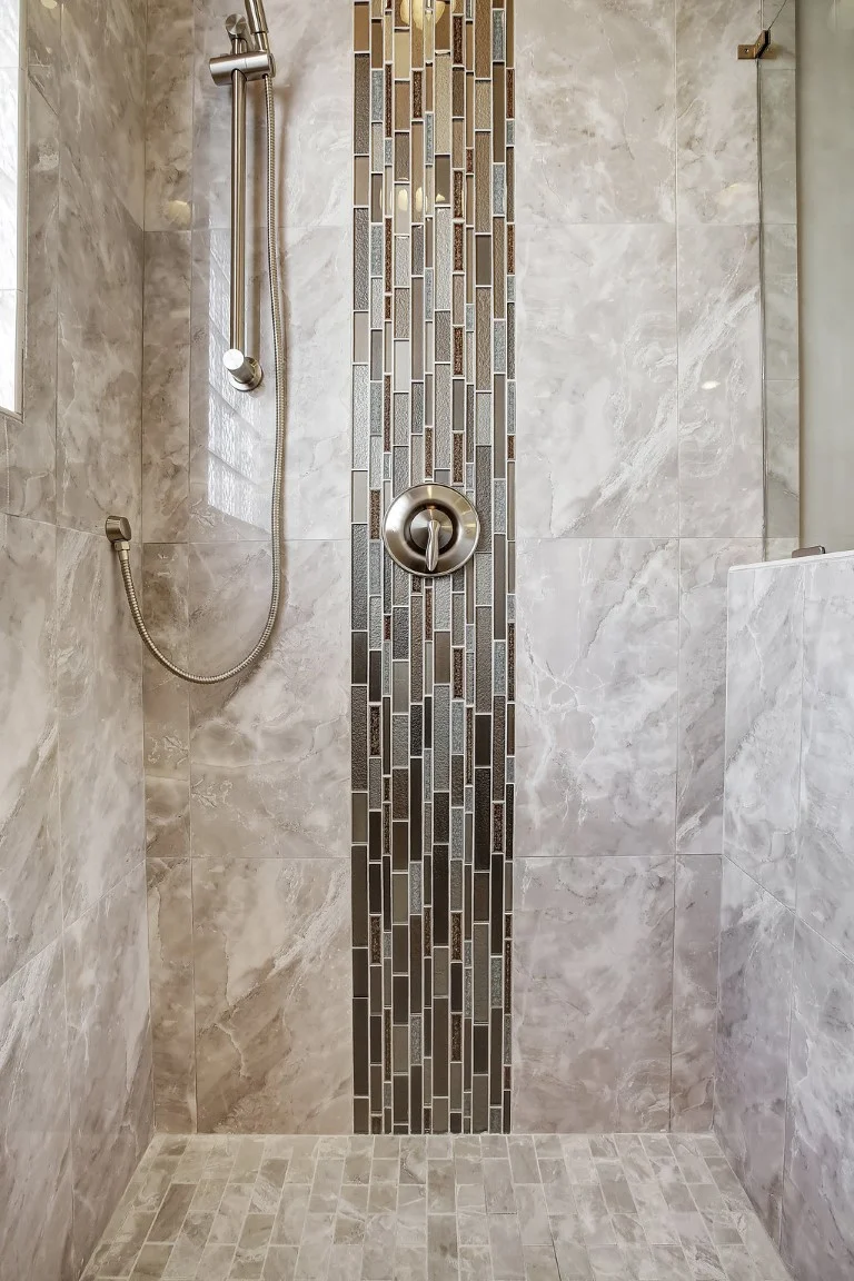 Marble-tiled shower with vertical mosaic accent and sleek fixtures, showcasing modern design by a home builder.